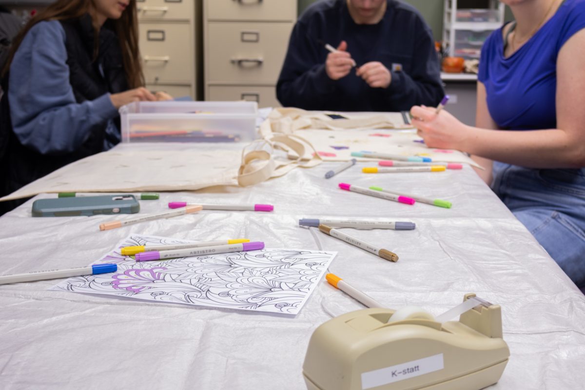 Paint markers, colored pencils, coloring pages, totes and other materials scatter the table in the K-Statt while students decorate tote bags provided by EARTH Club.